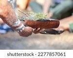 Small photo of Human hands hold wooden dish with Australian plant branches, the smoke ritual rite at a indigenous community event in Australia