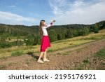 A young Ukrainian girl in a national suit stands in a meadow in the mountains, looking at the sky and asking for heaven, hands raised to the sky. Independence Day.