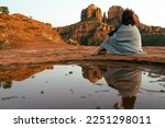 Small photo of Close up view of young brunette woman 30s sitting by small pool of water on red slick rock Cathedral Rock in Sedona Arizona USA in background during sunset blue hour. Woman looking away from camera.