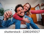Young caucasian couple showing keys of their first house after purchase and moving to new home together. happy husband and wife hugging in their apartment excited to be owners of a apartment. High