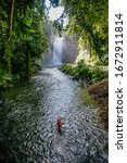 Small photo of A woman catching freshwater fish in a river. In the background is the majestic Hikong Alu waterfalls of Lake Sebu, South Cotabato, Philippines.