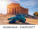 Bronze statue of Icarus in front of the Temple of Concordia at the Valley of the Temples. Temple of Concordia and the statue of Fallen Icarus, in the Valley of the Temples, Agrigento, Sicily, Italy.