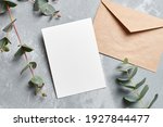 Wedding invitation card mockup with envelope and eucalyptus branches on grey concrete background, top view