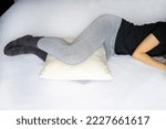 Leg cushion for sleeping for knee pain. Orthopedic pillow between the legs of a lying woman in pajamas.