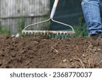 Small photo of Man raking soil in the garden. Metal garden rake. Loosening soil.