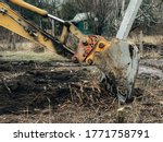 Excavator uprooting trees on land in countryside. Bulldozer clearing land from old trees, roots and branches with dirt and trash. Backhoe machinery. Yard work