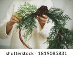 Rustic christmas wreath in female hands. Florist holding modern natural wreath with pine cone and cedar branches on white background. Seasonal holiday workshop or making wreath at home