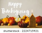 Happy Thanksgiving greeting card. Happy Thanksgiving text on pumpkins, candle, autumn flowers, berries, leaves composition on wooden table in rustic room. Handwritten lettering
