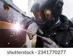 Shielded metal arc welding. Worker welding metal with electrodes, wearing protective helmet and gloves. Close up of electrode welding and electric sparks