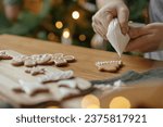 Hands decorating gingerbread cookies with icing on rustic wooden table at christmas tree golden lights. Atmospheric Christmas holiday traditions, family time