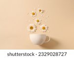 White cup and chamomile flowers on a blue background. Chamomiles come out of the cup like steam. Chamomile tea concept. Flat lay, top view.