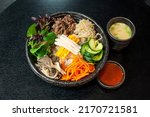 Korean Bulgogi Bibimbap, marinated beef bento box hot stone bowl with salads, kimchi, Bibimbap sauce, miso soup on black table background
