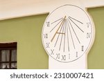 Small photo of Sundial on the wall of a historic building. A sundial with a copper (brass!?) gnomon ("hand" of the clock) hanging on a green (and white) wall.