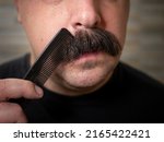Closeup of a young man brushing his thick black bushy mustache 