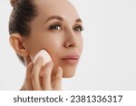 Small photo of Closeup portrait of a woman applying dry cosmetic tonal foundation using makeup sponge on the face using makeup brush.