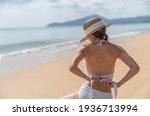 Back side woman in white bikini sitting on sand beach relaxing sunbathing.