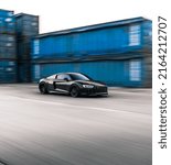 Small photo of Tacoma, WA, USA March 3, 2022 Black Audi R8 driving with blue shipping containers in the background