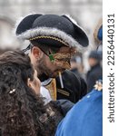 Small photo of Venice, Italy - 02.19.2022: Handsome young man in carnival mask wearing tricorn with an unlit cigarette in his mouth at Venice carnival among his friends