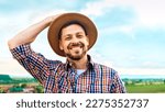 Small photo of Portrait of handsome Caucasian cheerful man in motley shirt taking off hat like greeting gesture and smiling to camera in field. Happy male shepherd at grassland. Close up. Outdoors.
