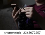 Small photo of Girl holding smartphone in her hand, watching crocheting tutorial and learning how to crochet. Fingers of a young lady holding crochet hook and wool thread. Girls hands crocheting handmade jacket.