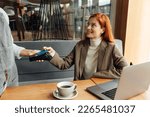 Smiling businesswoman with ginger hair paying by card in coffee shop