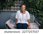 Small photo of Happy mature woman on a bench. Smiling woman with short hair relaxing in backyard.