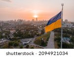 Aerial view of the Ukrainian flag waving in the wind against the city of Kyiv, Ukraine near the famous statue of Motherland at sunset.