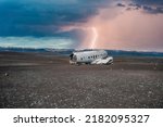 Lightning over broken military airplane wreck at black sand beach. Abandoned airplane in Solheimasandur against stormy sky. Scenic view of tourist attraction on volcanic landscape against cloudscape.