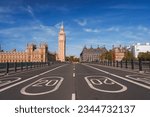Empty road leading towards Big Ben and Westminster palace. Numbers and signs on bridge during sunny day. Famous tourist attraction with blue sky in background.