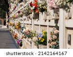 Small photo of Italian wall cemetery with tombstones and artificial flowers on a sunny summer day in Venice, Italy, Island of San Michele. Commemoration of the dead, deaths of pandemic.