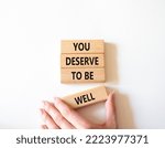 Small photo of You deserve to be well symbol. Wooden blocks with words You deserve to be well. Beautiful white background. Businessman hand. You deserve to be well concept. Copy space.
