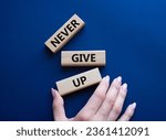 Small photo of Never give up symbol. Concept words Never give up on wooden blocks. Beautiful deep blue background. Businessman hand. Business and Never give up concept. Copy space.