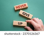 Small photo of Never give up symbol. Concept words Never give up on wooden blocks. Beautiful grey green background. Businessman hand. Business and Never give up concept. Copy space.
