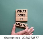 What does it mean symbol. Wooden blocks with words What does it mean. Beautiful grey green background. Businessman hand. Business and What does it mean concept. Copy space.