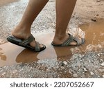 Small photo of The feet of a girl walking on the croon water on the road. walking on a muddy road.