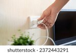 Small photo of Hand ready to plug or unplug white power cord cable mobile phone charger charts Into electric socket on wall. Electricity charger concept.