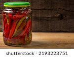 Marinated hot peppers in jar over wooden background