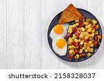 Small photo of Corned Beef Hash Browns with sunny side up fried eggs and toasted rye bread on plate on white wood table, horizontal view from above, flat lay, free space