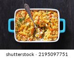 Chicken Pot Pie Fusilli pasta Bake with celery, corn, green peas, carrots , topped with panko breadcrumbs in baking dish on dark wood table, horizontal view from above, flat lay, close-up
