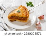 slice of  Ground Beef Meat Pie with a flaky puff pastry double crust with hearty minced beef cooked with vegetables and seasoning in white baking dish on wood table