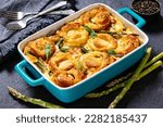 Small photo of asparagus ham strata topped with sponge cake circles in baking dish on concrete table with forks