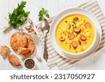 Kartoffelsuppe, German creamy potato soup with sausages in white bowl on white wooden table, flat lay