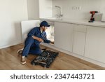 Professional plumber in blue uniform fixing broken water tap in kitchen. Repair service concept