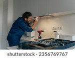 Professional male worker in uniform repairing modern cooker hood in kitchen