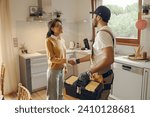 Professional repairman in uniform shaking hands with woman while standing at home kitchen