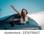Happy young pretty woman holding hands to the side and leaning out of car side view window. Travel adventure drive, happy summer vacation concept