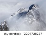 Dramatic, rocky, snowy mountain peak ridge in between mist and clouds, High Tatras, Lomnicky Peak, Slovakia, European alps. 