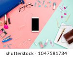 Business frame flatlay with woman's blue purse, glasses, smartphone with black copyspace, cosmetics and stationary supples. Pastel pink and mint background, mockup, women work bag contents
