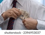 Small photo of An elegantly dressed man puts a wad of banknotes into his shirt pocket