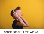 Small photo of Happy styli little boy in white headphones against yellow background.